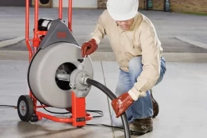 A man in white hard hat and beige shirt working on a pipe.
